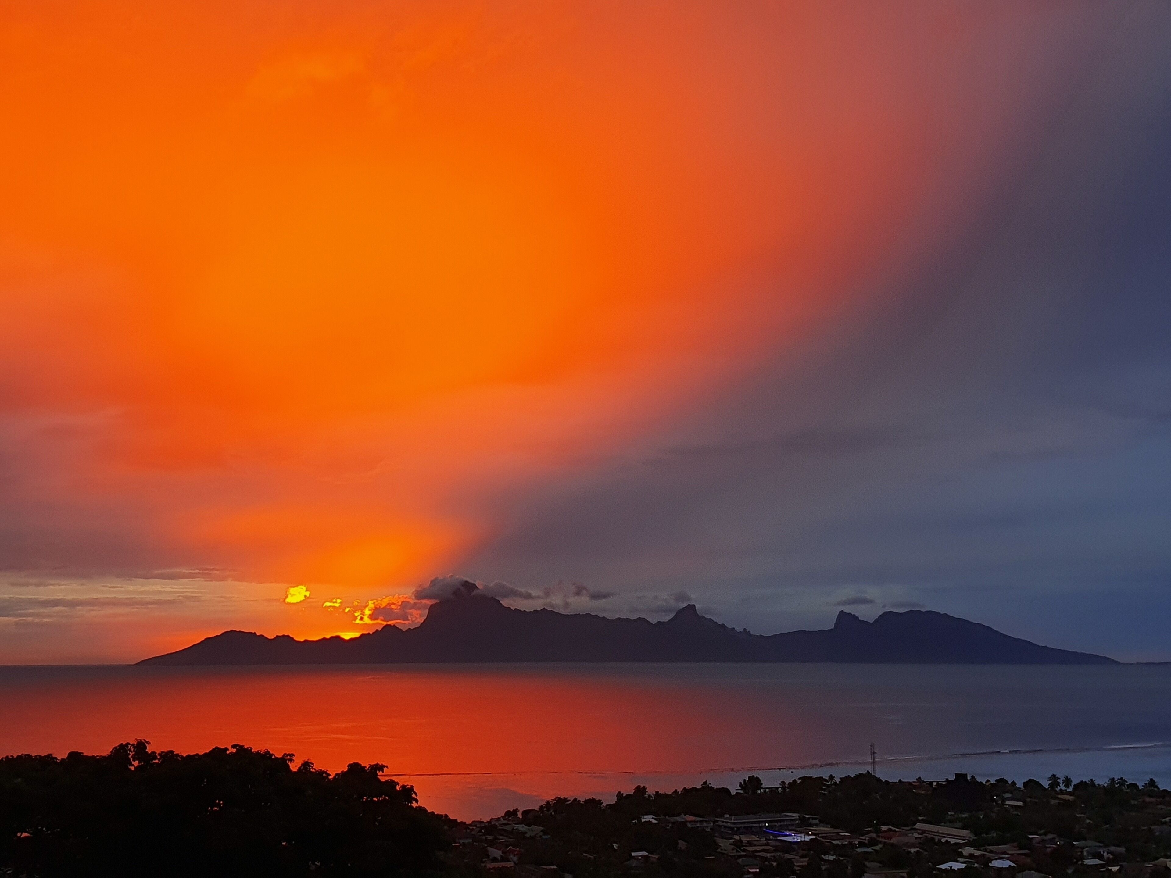 A sunset over a coastal landscape with mountains in the background.