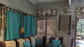 Una habitación rústica de madera con un sofá grande, cortinas color verde azulado y una pequeña mesa de madera con un libro.