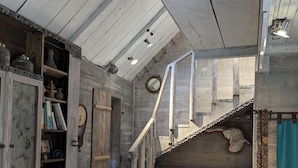 Un interior rústico con paredes de madera, una escalera, un sofá con cojines y un tambor.