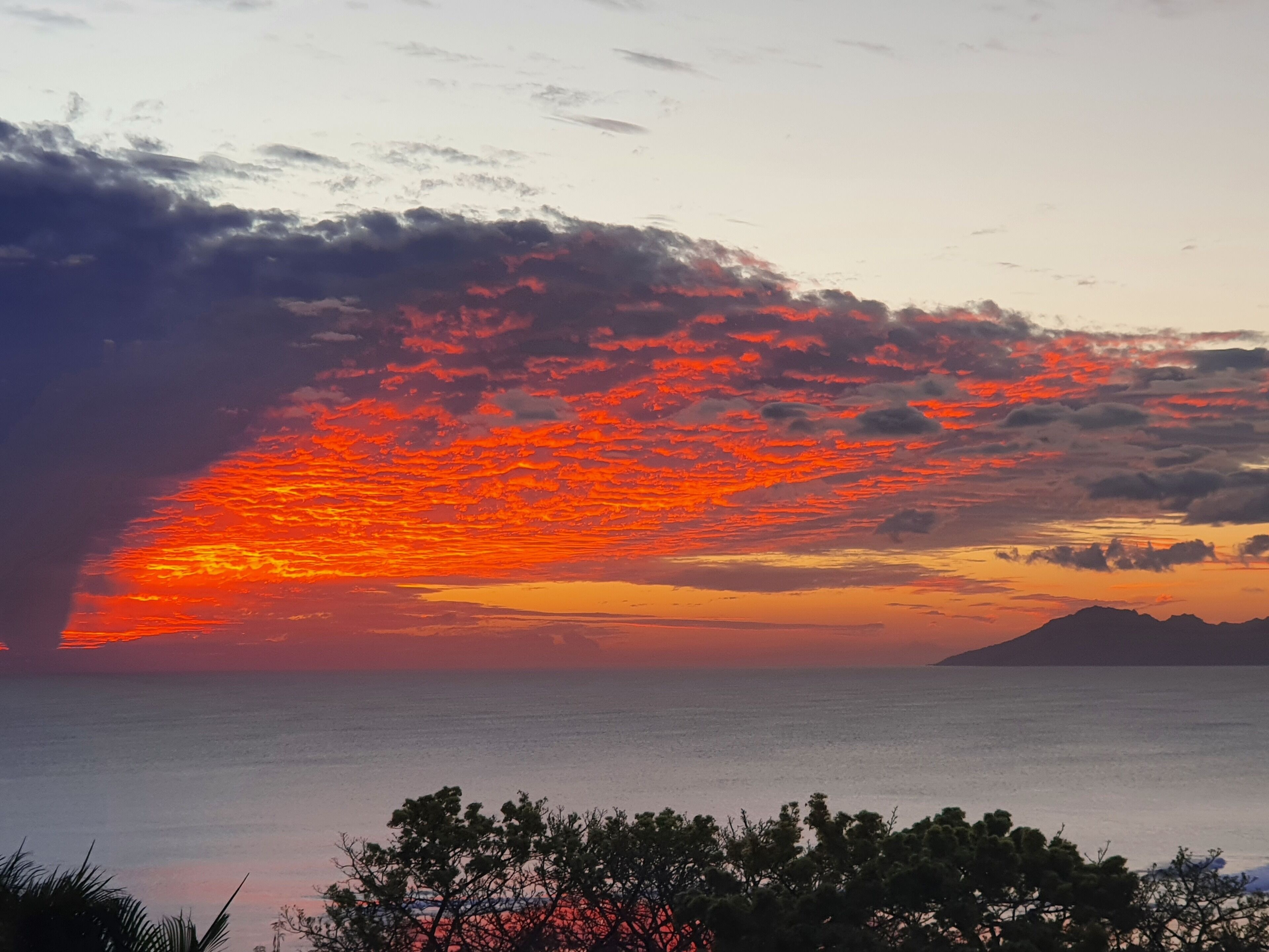 Un atardecer sobre un mar tranquilo con una cadena montañosa en la distancia.