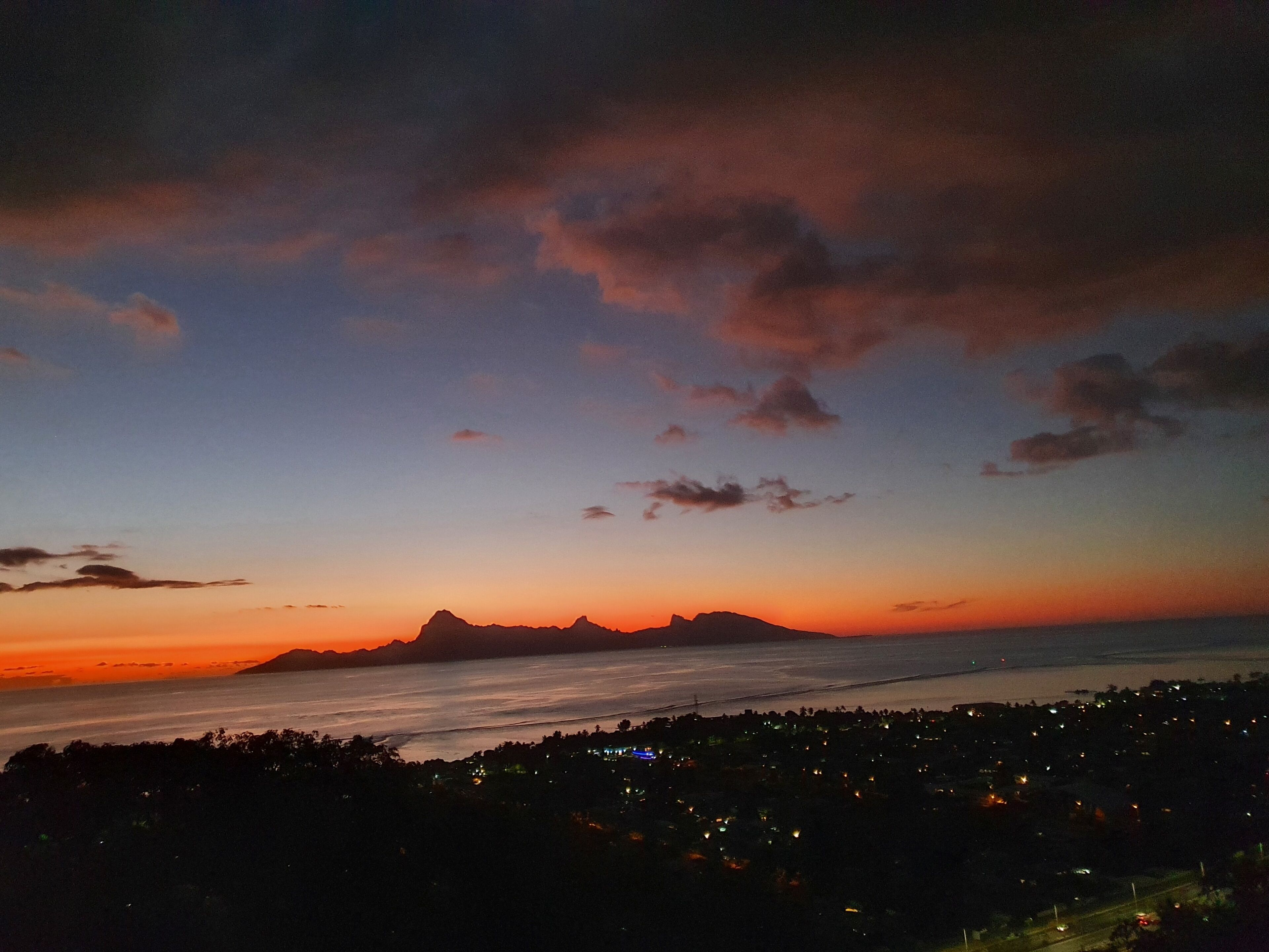 Un paysage côtier au crépuscule, avec une chaîne de montagnes à l’horizon et une vue sur la ville au premier plan.