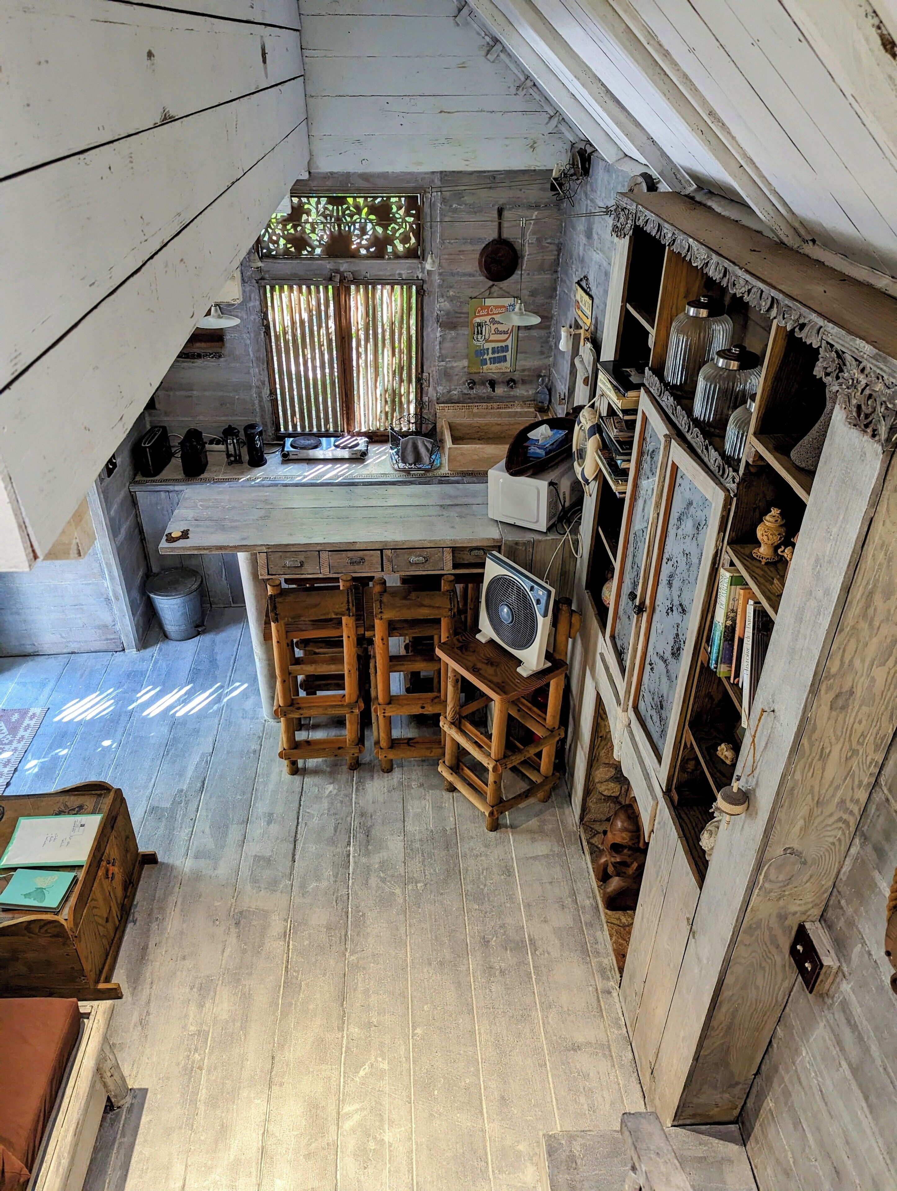 Une cuisine rustique avec un bar en bois, un ventilateur et des étagères remplies de divers objets.