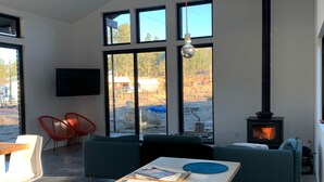 A modern living room with a large window, a fireplace, and a ceiling fan. - New Modern Home on Sylvan Lake Road (Custer)