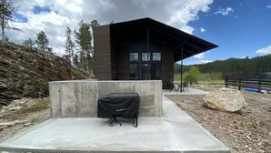 A modern building with a concrete patio, a grill, and a view of a forested area. - New Modern Home on Sylvan Lake Road (Custer)