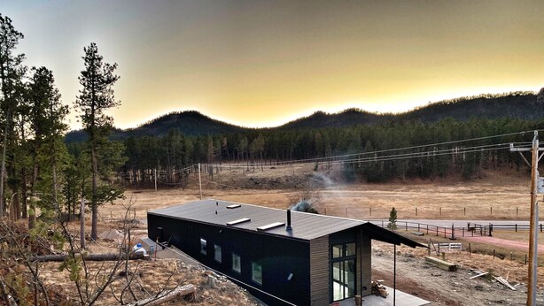 A modern house with a black exterior, large windows, and a chimney. - New Modern Home on Sylvan Lake Road (Custer)