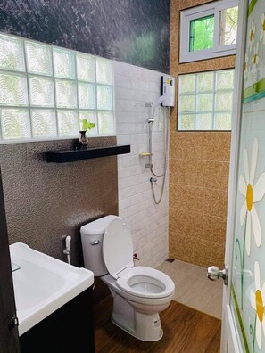 Ein Badezimmer mit Toilette, Dusche und Waschbecken. Ein Fenster bietet Blick auf Bäume.