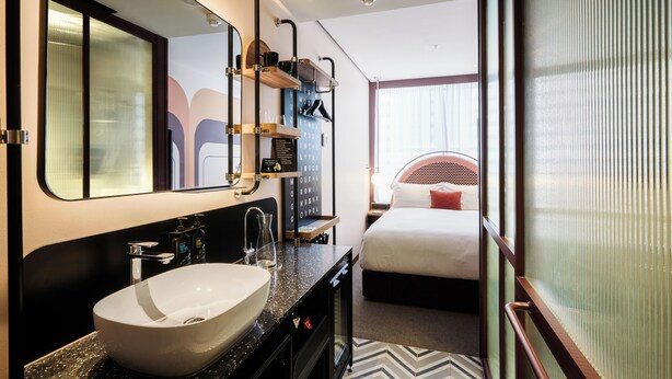 Hotelkamer met een groot wit wastafel, een spiegel, een bed met een rood kussen en een raam met uitzicht.