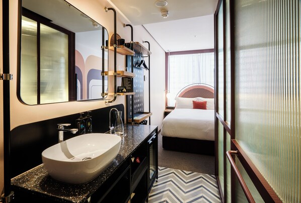 A hotel room with a large white sink, a mirror, a bed with a red pillow, and a window with a view.