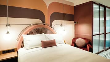 A modern hotel room with a bed, bedside tables, a red armchair, and a large window.
