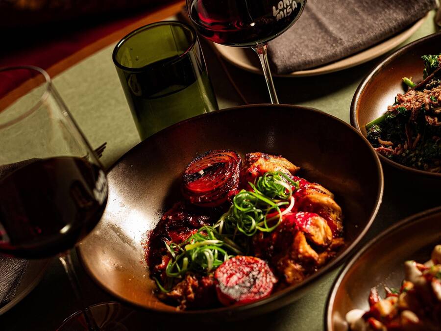A dining table with a variety of dishes, a glass of red wine, and a green glass.