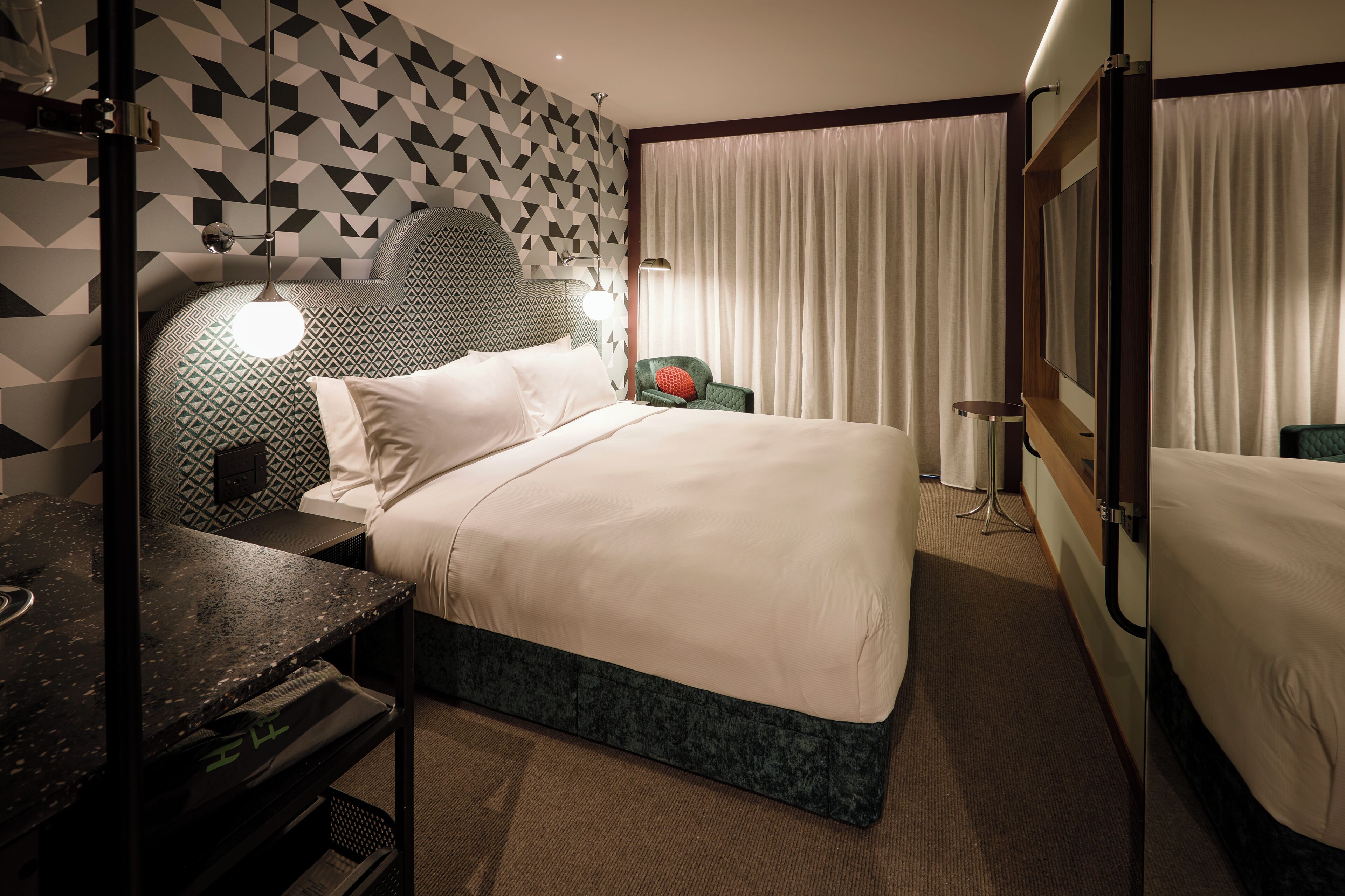 Habitación de hotel con cama, escritorio, silla, televisión y ventana con cortinas.
