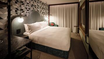 Habitación de hotel con cama, escritorio, silla, televisión y ventana con cortinas.