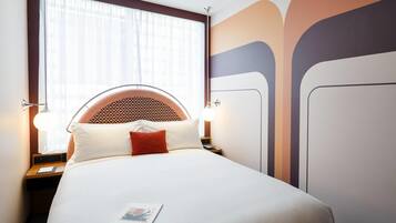 A hotel room with a bed, a nightstand, a lamp, and a window with curtains.