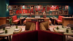 Een restaurant met rode fluweelzitzakken, een wand met ingelijste foto's en een gedekte tafel met wijnglazen en borden.