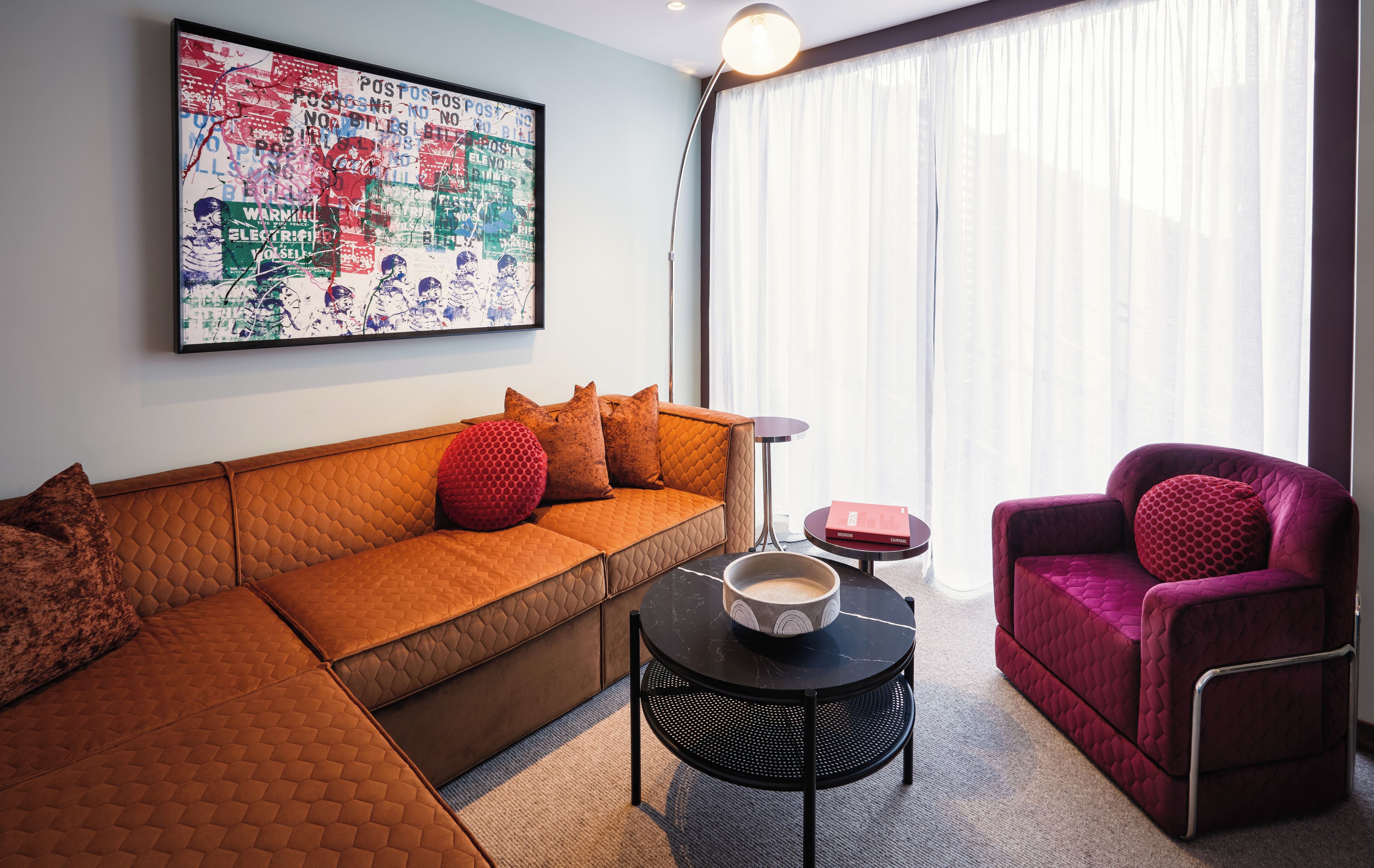 A modern living room with a sectional sofa, a red armchair, a round coffee table, and a large abstract painting on the wall.