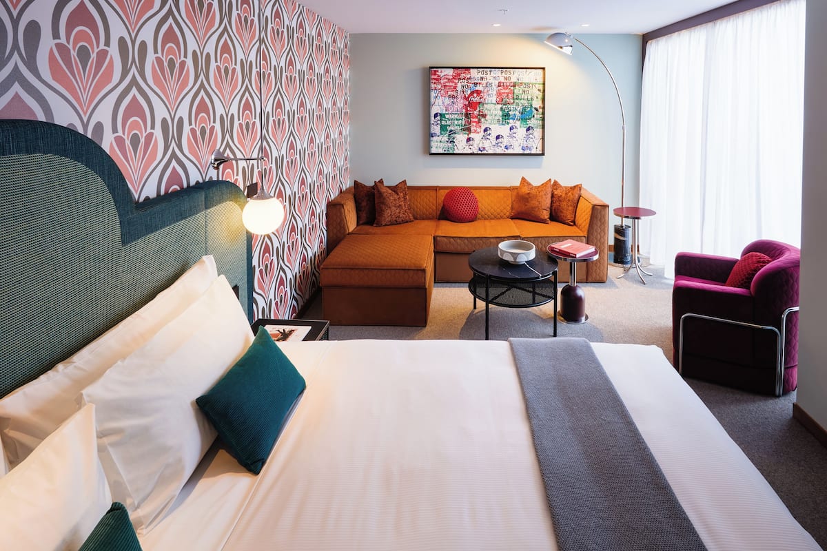 Una habitación de hotel moderna con una cama grande, un sofá, una mesita y una silla.
