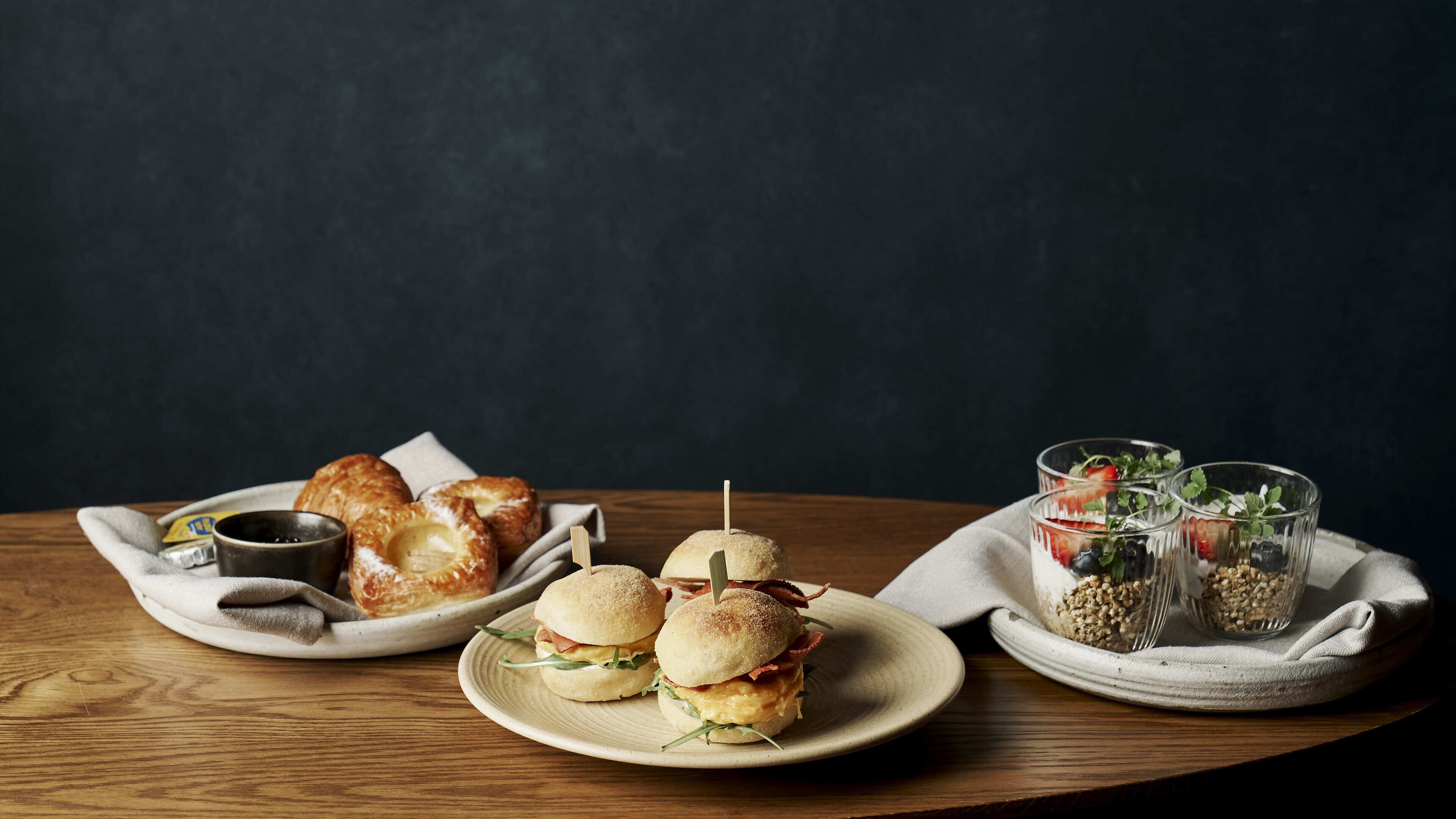 A wooden table with food items including sandwiches, pastries, and a drink.