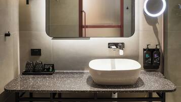 Un baño moderno con un espejo redondo, un lavabo blanco y un mueble de tocador con encimera moteada.