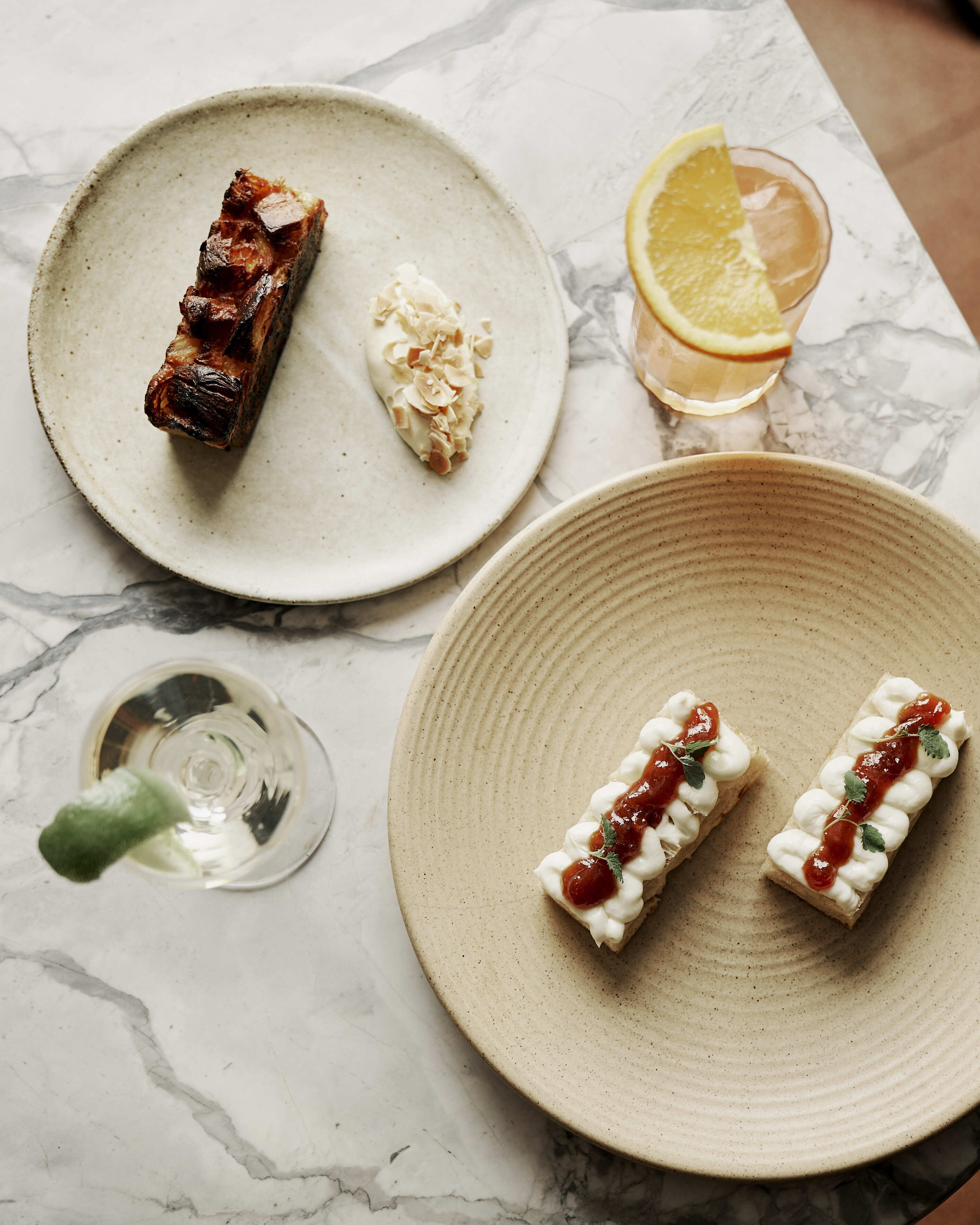 A marble table with four plates of food, a glass of drink, and a bottle of water.
