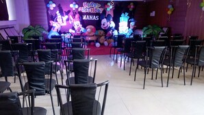 A room with rows of black chairs, a stage with a 'Happy Birthday Manas' backdrop, and balloons. - Hotel Sai Vijay (Nashik)