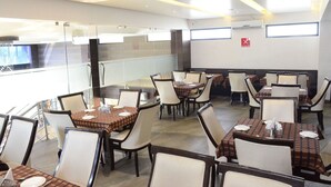 A restaurant with multiple tables and chairs, a glass partition, and a fire extinguisher on the wall. - Hotel Sai Vijay (Nashik)
