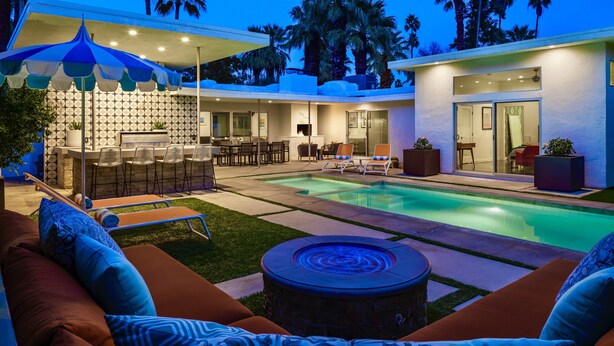 Un área de piscina exterior moderna con un bar, asientos y un patio bien iluminado.