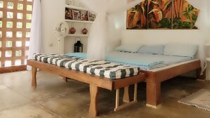 Une pièce comprenant un lit, un ventilateur, une étagère avec des objets décoratifs et une fenêtre avec des rideaux.