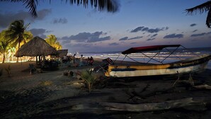 Une scène de plage avec une hutte au toit de chaume, un bateau et des palmiers.