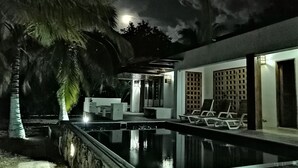 Un espace piscine aménagé pour la nuit, offrant une vue dégagée sur la piscine, les chaises longues et un palmier.