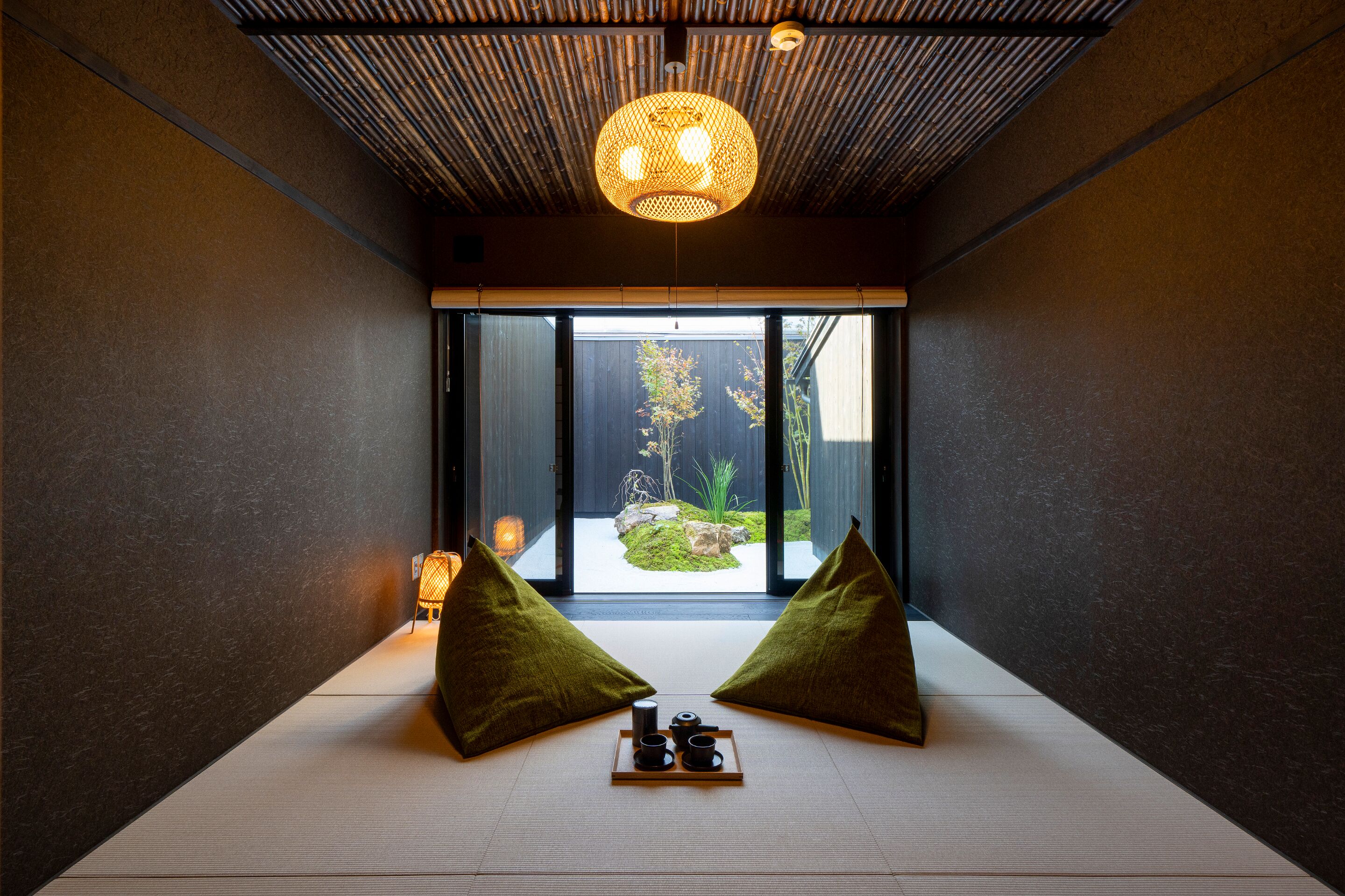 A minimalist room with tatami flooring, a traditional Japanese lantern, and a view of a garden through large sliding doors.
