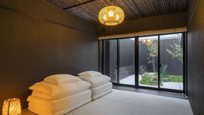 A modern room with tatami flooring, a large window with a view of a garden, and a stack of white pillows. - Sanjusangendo Yoinotake (Kyoto)