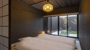 A modern bedroom with a large bed, a view of a garden through a sliding door, and a unique ceiling light fixture. - Sanjusangendo Yoinotake (Kyoto)