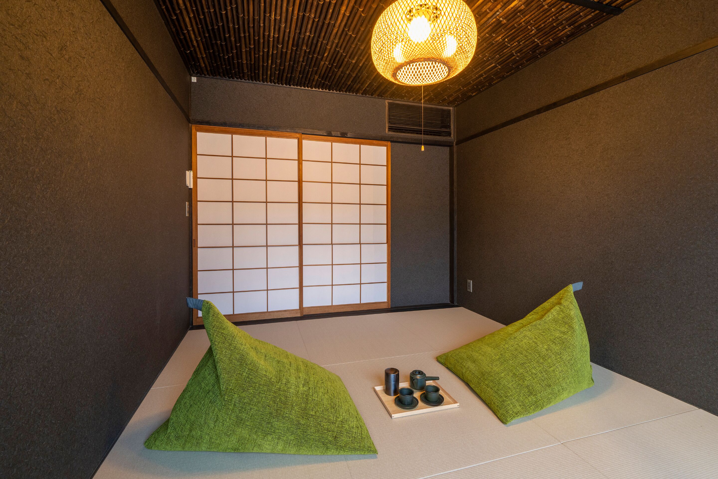 A traditional Japanese room with tatami flooring, shoji screens, and a hanging light fixture.