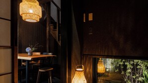 A dimly lit room with a wooden table and chairs, a woven floor mat, and two hanging lamps. - Sanjusangendo Yoinotake (Kyoto)