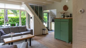 Un espace de vie moderne avec un escalier menant à un niveau supérieur, une cuisine aux couleurs vertes et un coin salon comprenant un canapé et une table basse.