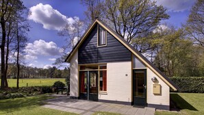 Une maison à deux étages, avec un toit foncé, des murs de couleur beige et un petit porche à l’avant.