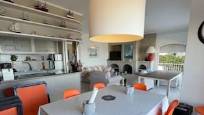 Un coin repas avec une table et des chaises, une cuisine avec des meubles blancs et un salon avec un canapé et une cheminée.