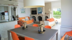 Un salon moderne comprenant un canapé, un téléviseur, une cheminée et un coin repas avec des chaises et une table orange.