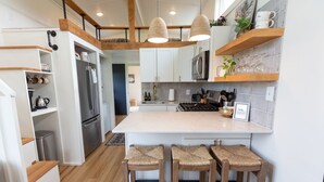Una cocina moderna con armarios blancos, una isla central con taburetes, vigas de madera e iluminación colgante.