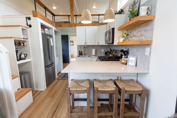 A modern kitchen with white cabinets, a central island with stools, wooden beams, and hanging pendant lights.
