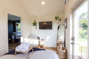 Un dormitorio moderno con cama, escritorio, silla y televisor. Hay plantas y una ventana con vistas.