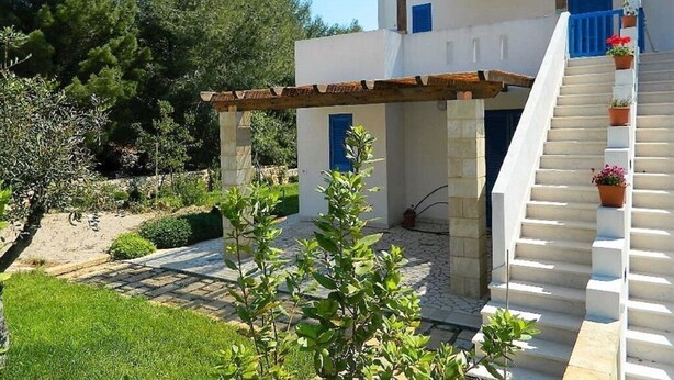 A two-story building with a white exterior, a wooden pergola over the entrance, and a staircase leading to the upper floor. - Il Carrubo bright and fresh apartment with beautiful view (Marina di Novaglie)