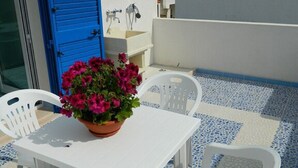 A white table with a potted plant, white chairs, and a blue and white tiled floor. - Il Carrubo bright and fresh apartment with beautiful view (Marina di Novaglie)