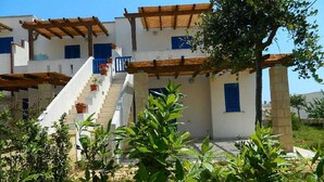 A multi-story building with white walls and blue shutters, featuring a staircase with potted plants and a pergola structure. - Il Carrubo bright and fresh apartment with beautiful view (Marina di Novaglie)