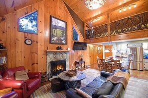 Ein gemütliches Blockhaus-Interieur mit Kamin aus Stein, Ledermöbeln, einer Essecke und einer Küche mit Edelstahlgeräten.