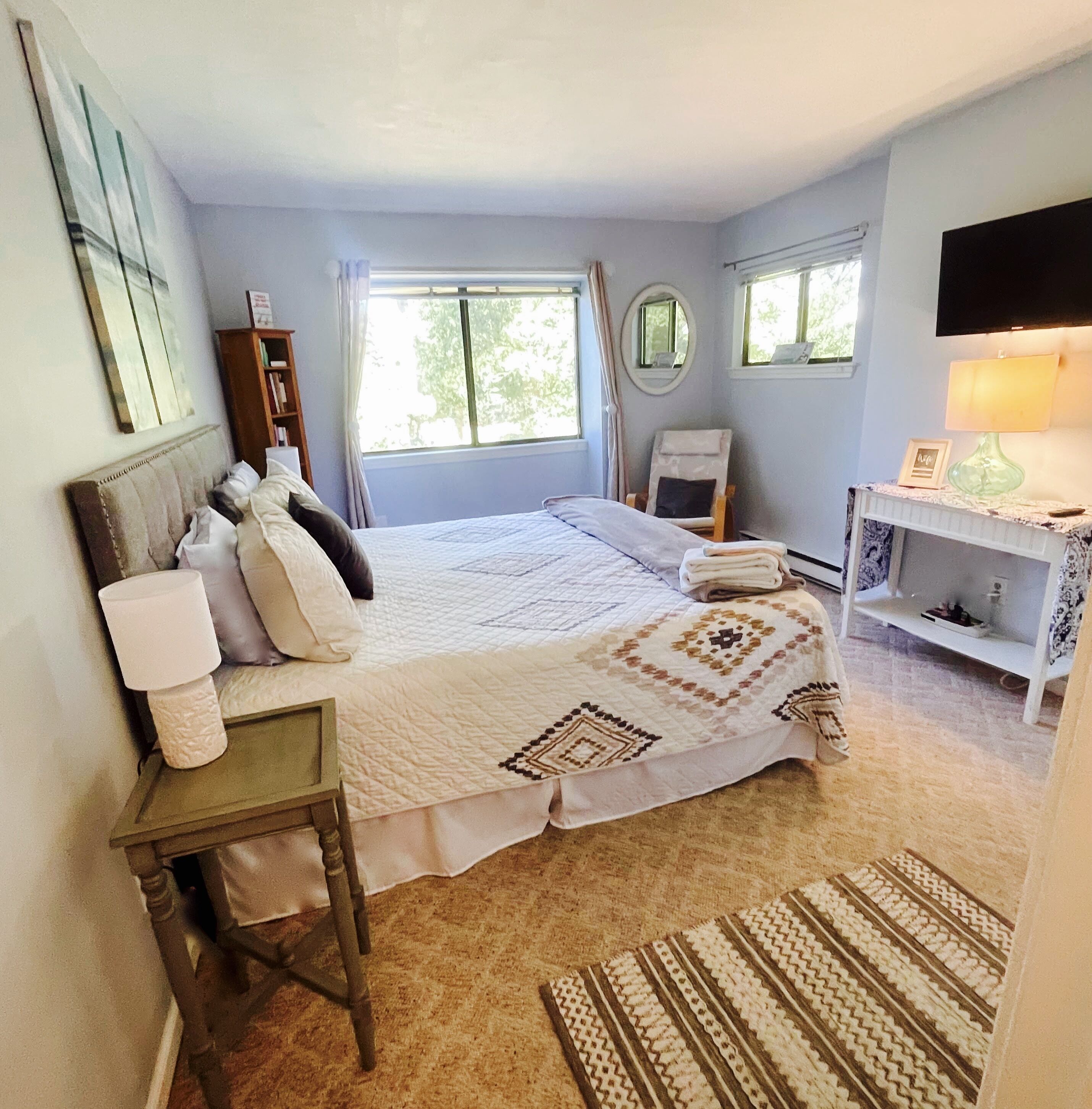 A bedroom with a bed, bedside table, lamp, chair, and a small desk with a lamp.
