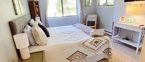 A bedroom with a bed, bedside table, lamp, chair, and a small desk with a lamp.