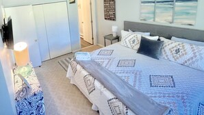 A bedroom with a large bed, a bedside table with a lamp, a wardrobe, and a view of the ocean through a window.