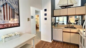 A modern kitchen with a built-in dishwasher, a small dining area with a white table, and a large window above the sink.