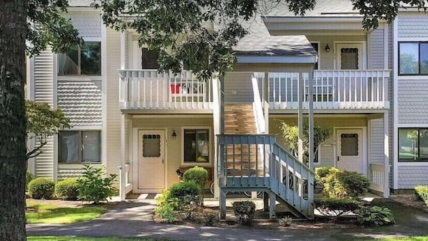 A two-story residential building with a central staircase, a covered porch, and a small front yard with landscaping.